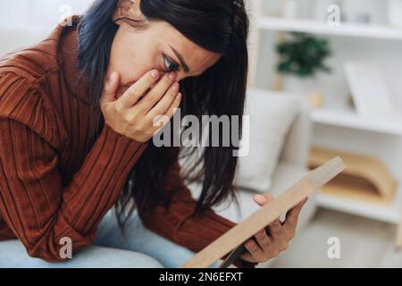 The woman looks sadly at the picture frames in her hands and with memories, a state of depression and loss of a person Stock Photo