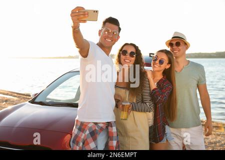 Happy friends taking selfie near car on beach. Summer trip Stock Photo