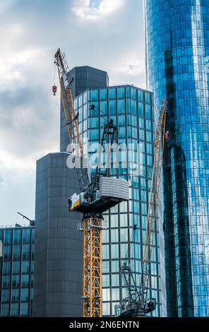Construction cranes in front of several skyscrapers of different heights. Vertical. Stock Photo