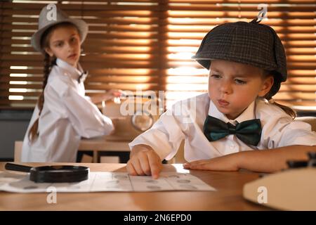 Cute little detective exploring fingerprints while her colleague switching on radio in office Stock Photo