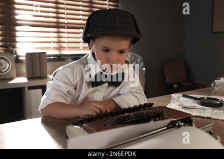 Cute little detective using typewriter at table in office Stock Photo