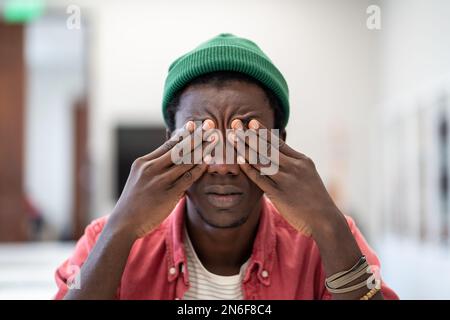 Tired stressed African guy student sitting in library massaging eyes feeling unmotivated to study Stock Photo