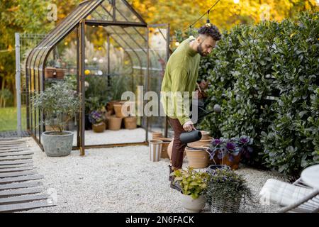 Stylish guy with watering can in garden Stock Photo