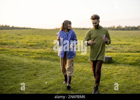 Couple hang out together, walking on green field on sunset Stock Photo