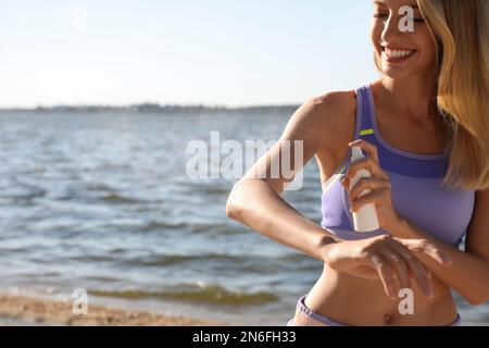 Young woman using insect repellent near sea on sunny day Stock Photo