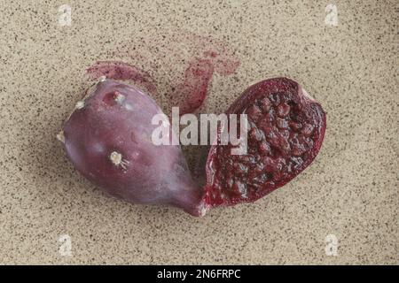 closeup of a edible red opuntia ficus-indica indian fig cactus fruit that is cut open on a beige ceramic plate showing juice and seeds that look like Stock Photo