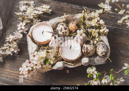 Candles in eggshells, quail eggs and white blossoming apple tree branches on a wooden tray as an Easter decoration, top view Stock Photo
