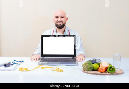 Nutritionist man showing laptop screen. Nutritionist at desk showing blank screen of laptop. Smiling nutritionist showing an advertisement on the Stock Photo