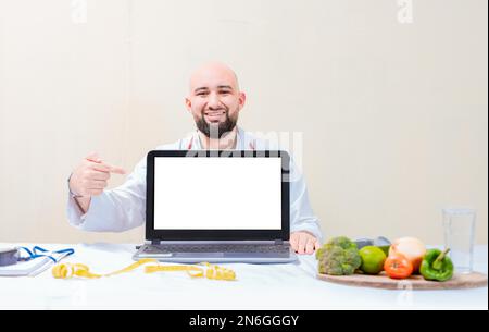 Smiling nutritionist pointing at an advertisement on the laptop, Nutritionist man pointing at laptop screen. Professional nutritionist pointing at Stock Photo