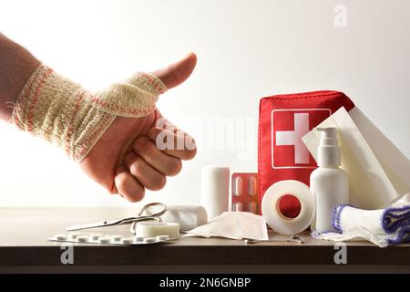Emergency home kit on wooden table and bandaged hand with ok gesture isolated background. Horizontal composition. Front view. Stock Photo