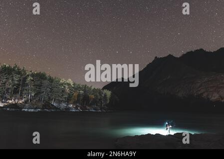 The silhouette of a fisherman girl with a lantern waves a fishing rod at  night on the river bank under a rock with stars in Altai Stock Photo - Alamy