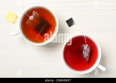 Different tea bags in cups of hot water on white wooden table, flat lay Stock Photo