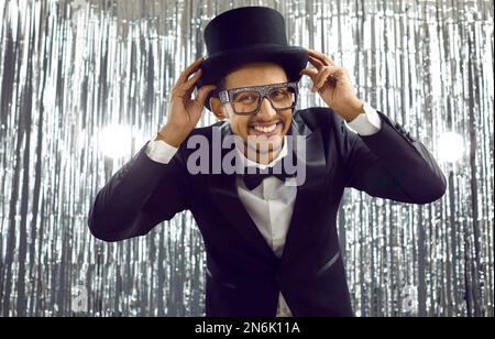 Funny young black man in a dinner suit, top hat and glasses having fun at a party Stock Photo