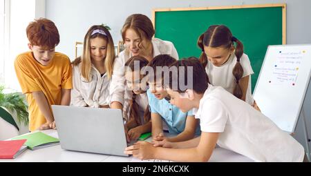 Children in class at elementary school with teacher working together on laptop in classroom. Stock Photo