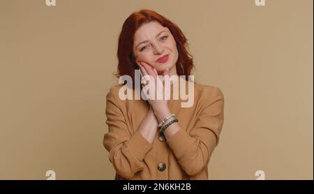 Hipster redhead woman touching sore cheek suffering from toothache cavities or gingivitis waiting for dentist appointment gums disease. Young girl indoor studio shot isolated alone on beige background Stock Photo