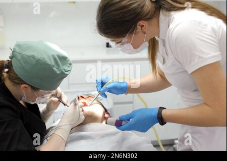 dentistry doctor treats a tooth in man patient women in masks on them sterile gloves smart watch modern technology dental treatment tooth extraction hurt teeth cleaning teeth dental office Stock Photo