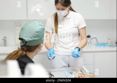 medical workers in dentistry decide and choose Which instrument to use in process of dental treatment female nurse asks teacher doctor woman showing printed sterile disposable packaging instrument Stock Photo