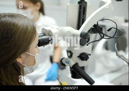 Modern dental equipment Medium shot of female dentist mask gloves using dental microscope to examine patients teeth doctor patient assistant dental tr Stock Photo