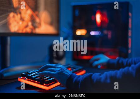Close up of pro gamer's hands on keyboard in neon color, blur background. First-Person Shooter. Professional cyber sport gamer playing online video games at home, takea part in tournament. Soft focus. Stock Photo