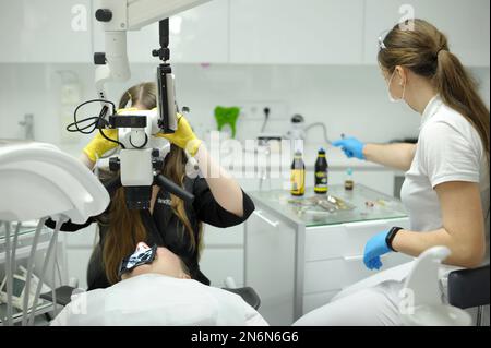 Modern dental equipment Medium shot dentist mask gloves using dental microscope to examine patients teeth doctor patient assistant dental treatment pr Stock Photo