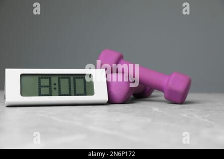 Alarm clock and dumbbells on table against grey background. Morning exercise Stock Photo