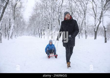 Father sledding his child outside on winter day. Christmas vacation Stock Photo