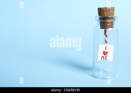 Piece of paper with phrase I Love Me in small glass bottle on light blue background, space for text Stock Photo