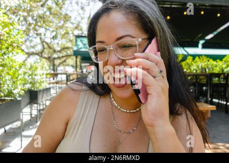 young latin woman of venezuelan ethnicity, with glasses and long hair, happy outdoors very pleased smiling on a phone call. Stock Photo