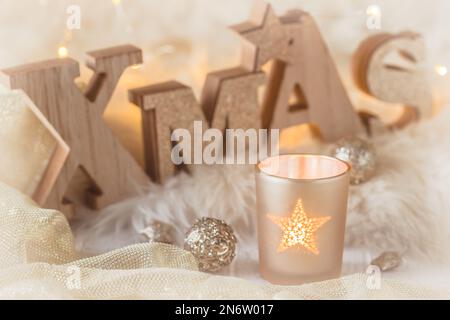 Small glass with tea light and word xmas in wooden capital letters, christmas decoration, and fairy lights on a white wood and white fur Stock Photo