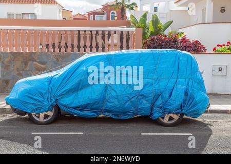 Car completely covered with a blue tarpaulin on a street in Corralejo, Fuerteventura. Stock Photo