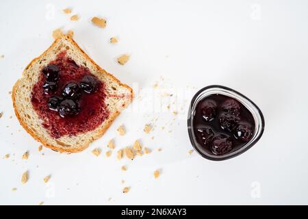 Homemade sour cherry jam, small bowl and a slice of bread with jam isolated on white background. Stock Photo