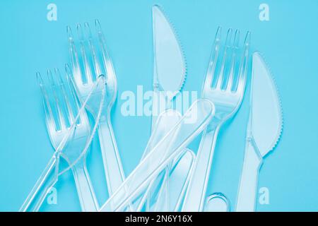 Plastic disposable tableware, cutlery. Fast food. Clean plastic forks and knives on blue background. Disposable dishes, environmental pollution. Top v Stock Photo