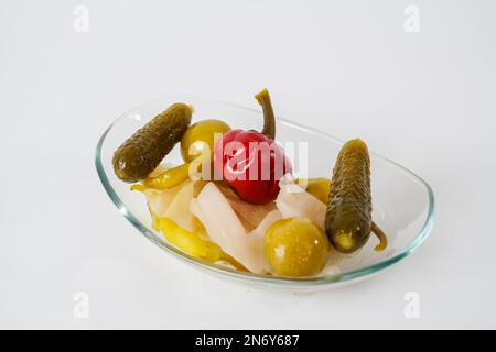 Mixed gherkins, sauerkraut, pepper, tomato and cucumber pickles on glass plate isolated on white background. Stock Photo