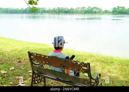 Man Sitting on the Lakeshore Bench Checking on His Smartphone Stock Photo