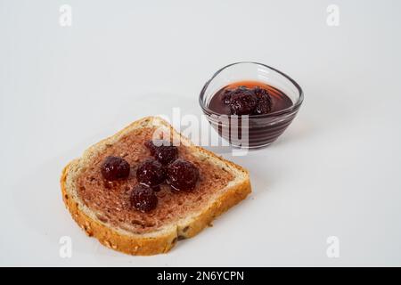 Homemade strawberry jam, small bowl and a slice of bread with jam isolated on white background. Stock Photo