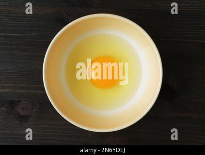Top View of a Fresh Raw Egg Yolk and White in a Bowl Isolated on Wooden Table Stock Photo
