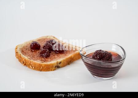 Homemade strawberry jam, small bowl and a slice of bread with jam isolated on white background. Stock Photo