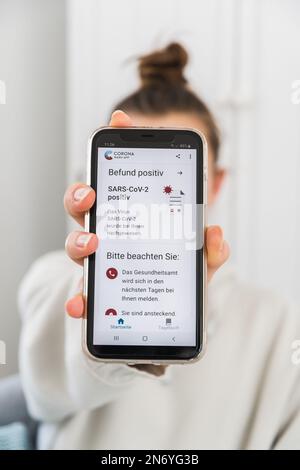 Germany - March 27th 2021: Official German Corona Warning App with a positive Covid-19 test result on a smartphone shown by young woman, vertical. Bef Stock Photo