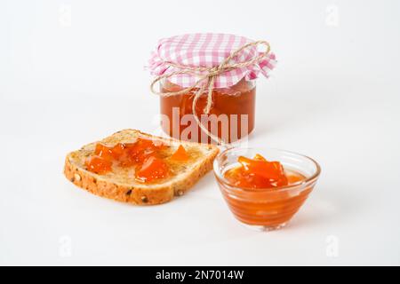 Homemade apricot jam, jar, small bowl and a slice of bread with jam isolated on white background. Stock Photo