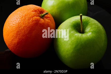 green apples and orange fruit. macro view. isolated fruits on black background in closeup. vitamins, healthy eating. vegetarian lifestyle. orange peel Stock Photo