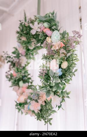happy easter and spring holidays time. easter wreath with sprigs of lilac bush blossom flowers and leaves and decorated colorful eggs on bright light Stock Photo