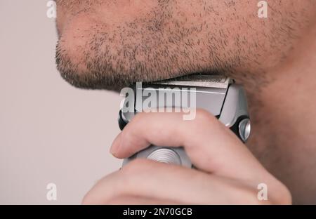 A man shaving his facial hair with an electric shaver. Close up. Stock Photo