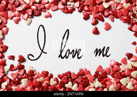 Handwritten phrase I Love Me and heart shaped sprinkles on white background, flat lay Stock Photo