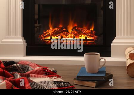 Cup of hot tea and books on floor near fireplace. Cozy atmosphere Stock Photo