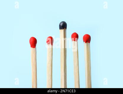 Row of whole matches and burnt one on light blue background. Uniqueness concept Stock Photo