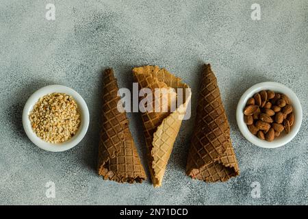 Overhead view of three empty waffle cones with bowls of almonds and chopped nuts Stock Photo