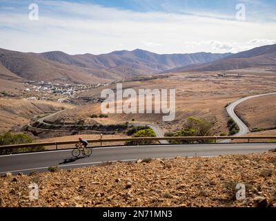 Road cyclist on narrow mountain road near viewpoint Mirador de Guise y Ayose, looking south to mountain village Betancuria, Canary Islands, Spain Stock Photo