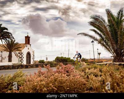 Racing cyclist passes church/hermitage of El Time: 'Ermita Säora de la Merced', Puerto del Rosario, Canary Islands, Spain Stock Photo