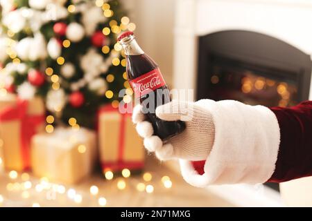 MYKOLAIV, UKRAINE - JANUARY 18, 2021: Santa Claus holding Coca-Cola bottle in room decorated for Christmas, closeup Stock Photo