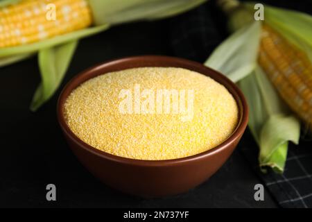 Cornmeal in bowl and fresh cobs on black table Stock Photo